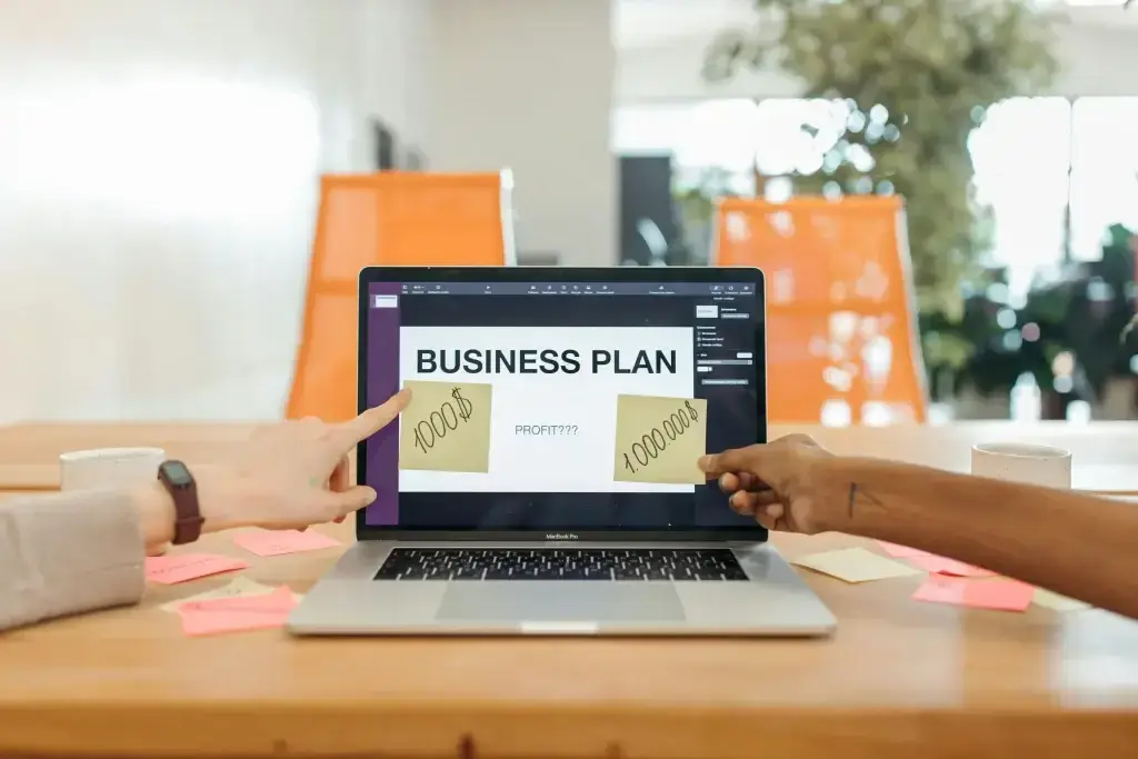 Two people discuss a business plan on a laptop screen that shows 'BUSINESS PLAN' and sticky notes with numbers in a bright office setting, including orange chairs in the background.”]}} }? Wait format must be array of strings. I should provide multiple strings. Let's redo. Provide 5 options. Ensure valid JSON. Let's output properly. Can only output the JSON object. Let's do. } I must ensure correct closing. Let's craft. JSON: {