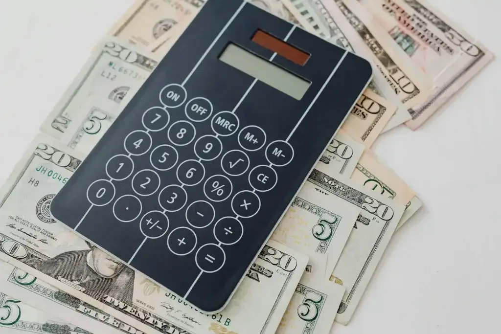 Calculator resting on a pile of US dollar bills, suggesting budgeting or financial calculations.